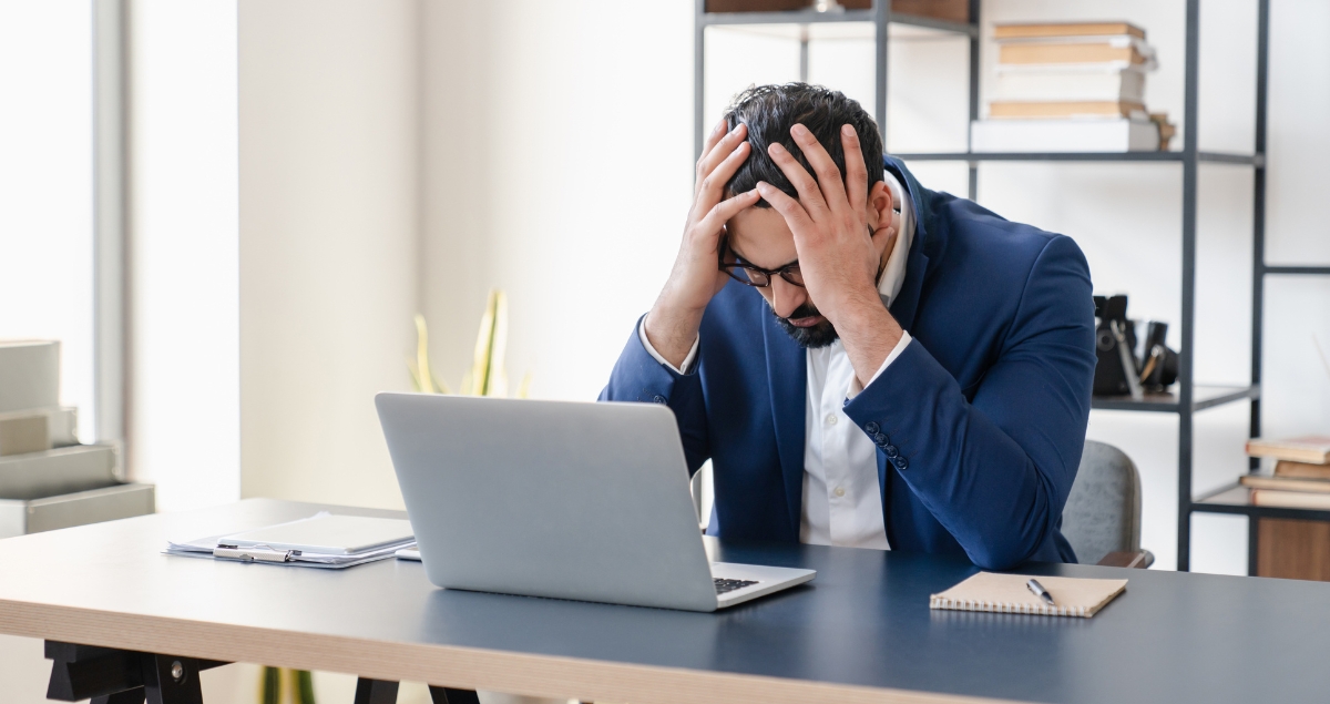 Frustrated man working on his computer with hands on his head.